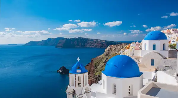 Santorini, idealne miejsce, gdzie na wakacje w sierpniu. Białe domy z niebieskimi kopułami nad lazurowym morzem.