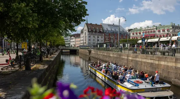 En paddanbåt med turister glider fram på kanalen i Göteborg. Blommor i förgrunden ger en färgklick.