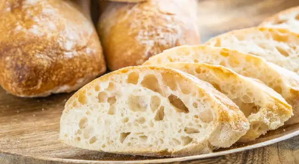 Frisch gebackene Ciabatta-Brote, aufgeschnitten auf einem Holzbrett. Das luftige Innere und die knusprige Kruste zeigen das gelungene Ciabatta Rezept.