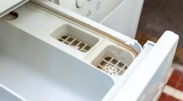 Schmutziges Waschmittelfach einer Waschmaschine, das dringend eine Reinigung benötigt. Kalk und Seifenreste haben sich abgelagert.