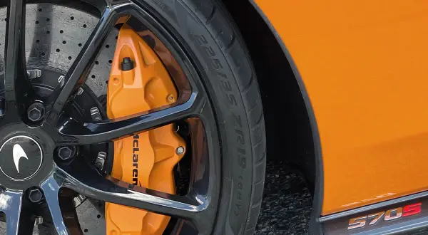 Pomarańczowy zacisk hamulcowy McLaren z oznaczeniami opon 225/35 ZR19 na czarnej feldze.