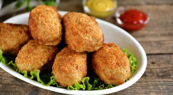 Six croquettes de crevette dorées et croustillantes sur un lit de laitue, avec des sauces moutarde et ketchup en arrière-plan.