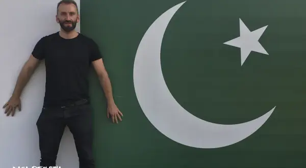 Mężczyzna w czarnym T-shircie i jeansach stoi obok flagi Pakistanu. Marzy o wizie do Pakistanu.