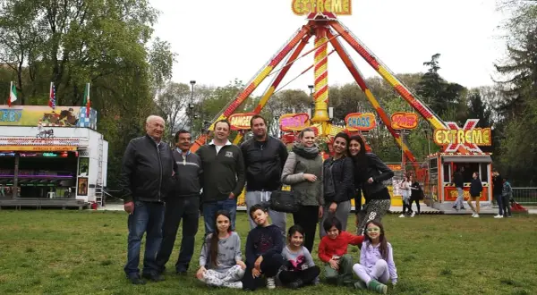 Famiglie giostrai italiani posano sorridenti davanti a un'attrazione "Extreme" in un parco divertimenti.
