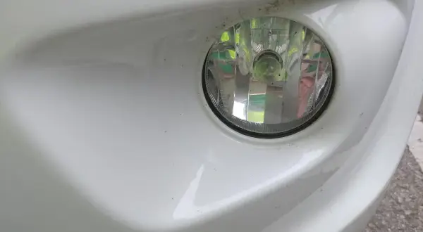 Zbliżenie na reflektor przeciwmgielny w białym zderzaku. Dowiedz się, jak włączyć światła przeciwmgielne, by poprawić widoczność.