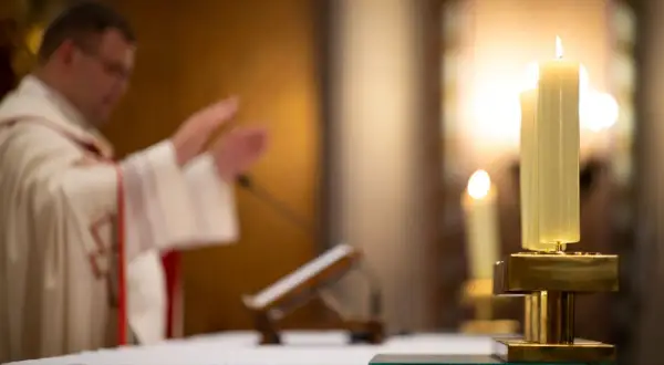 Ksiądz w kościele podczas mszy, zapalone świece. Czy księża płacą podatki? To pytanie nurtuje wielu.