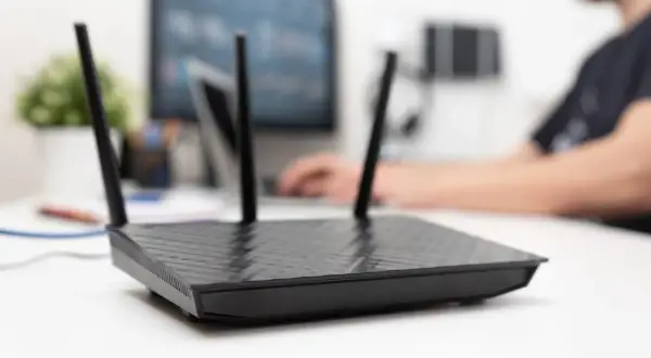 Czarny router z antenkami na biurku, obok monitora. Dowiedz się, jak aktywować kartę SIM w routerze, aby cieszyć się szybkim internetem.