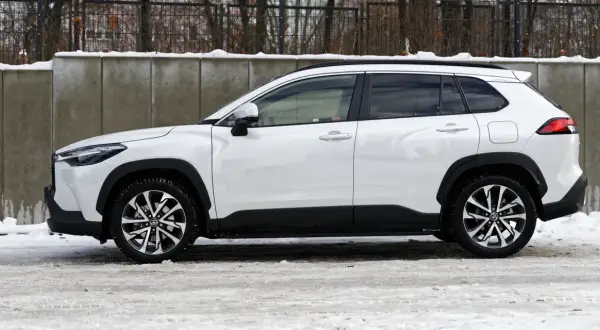 Biała Toyota Corolla Cross Hybrid na tle betonowego muru i śniegu. Stylowy SUV gotowy na zimowe wyzwania.