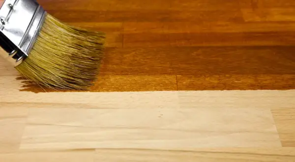Un pinceau applique un vernis pour foncer du bois, transformant le bois clair en une teinte chaude et profonde.