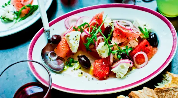 En läcker melon och fetaostsallad med oliver, rödlök och ruccola. Serveras med bröd och en kall dryck.