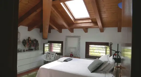 Camera da letto mansardata con travi a vista in legno. Idee colori per una mansarda luminosa e accogliente, con arredi bianchi e dettagli etnici.