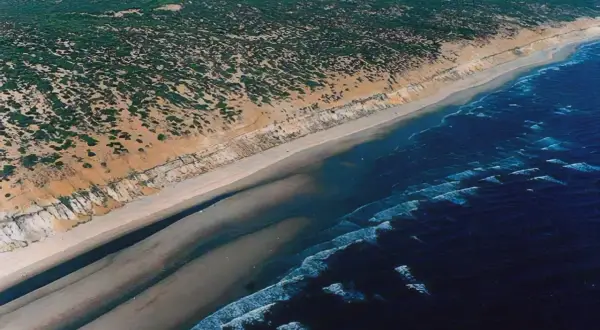 Vista aérea de la **playa de Castilla**, con dunas cubiertas de vegetación, arena dorada y el mar azul con olas.