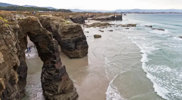 Impresionantes arcos de roca natural en la playa de Ribadeo, con el mar Cantábrico rompiendo suavemente en la arena.
