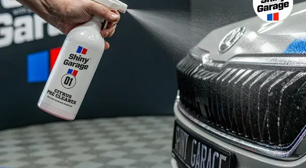 Ręka rozpyla pre-wash oprysk Citrus Pre Cleaner z butelki Shiny Garage na grill samochodu, usuwając brud.