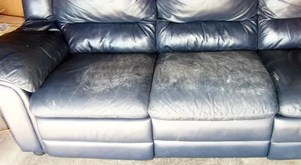 A dark blue leather couch with worn, scuffed seat cushions, showing the need for restoration.