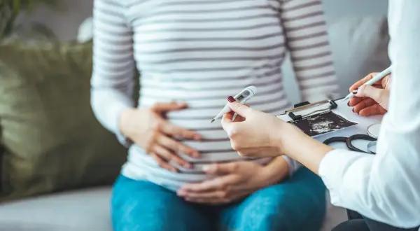 Lekarz bada ciężarną, trzymając termometr i USG. Ważne jest monitorowanie zdrowia w ciąży, aby wykluczyć np. cytomegalię.