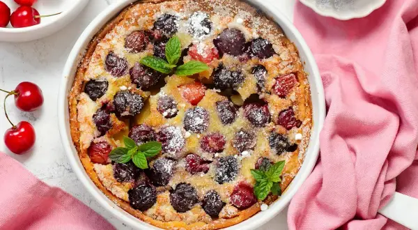 Clafoutis aux cerises, une recette de Laurent Mariotte, parsemé de sucre glace et décoré de feuilles de menthe.
