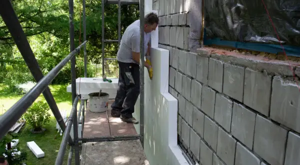 Pracownik montuje styropian na ścianie starego domu, pokazując, jak ocieplić dom.