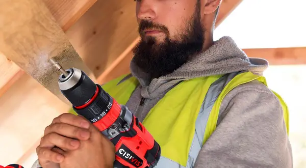 Operaio con barba usa un trapano per bucare mobile per cavi in legno.