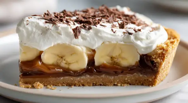 En bit krämig banoffee paj med lager av banan, kolasås och vispad grädde, toppad med chokladspån.