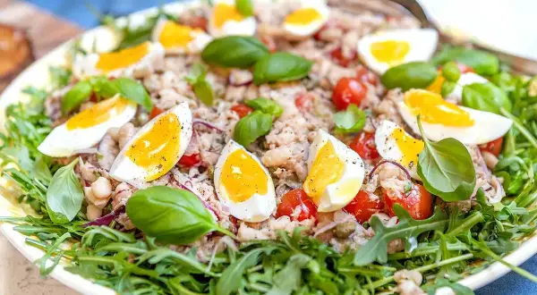 En härlig tonfisk sallad med kokta ägg, tomater, bönor och färsk basilika, serverad på en bädd av rucola.