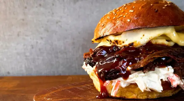 Saftiger pulled beef burger mit geschmolzenem Käse und BBQ-Sauce, serviert auf einem Holzbrett.