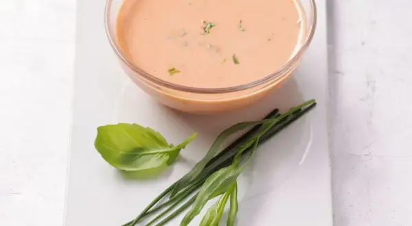Schüssel mit cremigem French Dressing, garniert mit frischem Basilikum und Schnittlauch.
