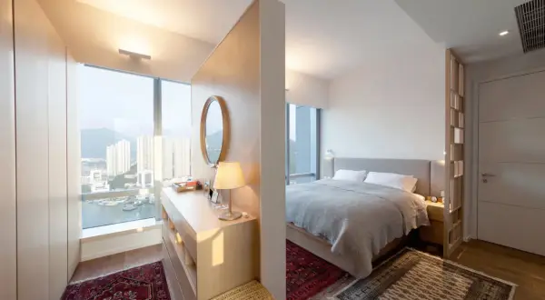 Ein moderner Schlafbereich mit einem Bett, getrennt durch einen eleganten raumteiler vorm bett, der auch als Schminktisch dient.