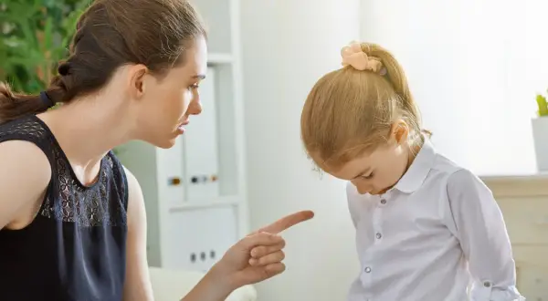 Matka karci córkę, wskazując palcem. Dziewczynka spuszcza wzrok, przyjmując konsekwencje swojego zachowania.
