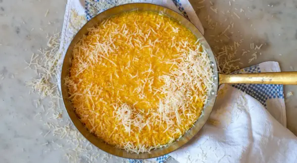 En gyllene risotto milanese, toppad med riven parmesan, i en metallpanna på en marmorskiva.
