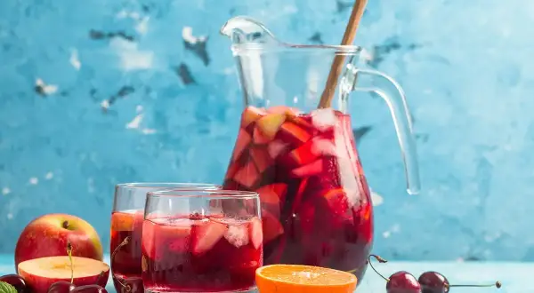 En karaff med röd bål fylld med frukt och is, serverad med två glas och färsk frukt. Perfekt för ett somrigt bål recept.