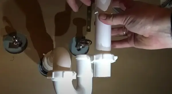 Hands assemble a white P-trap for a kitchen sink installation.