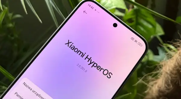 Ekran telefonu z napisem "Xiaomi HyperOS" w pastelowych barwach, otoczony zielenią roślin.