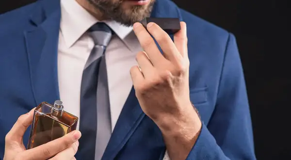 Elegancki mężczyzna w garniturze wącha perfumy. Czy to woda toaletowa czy perfumowana?