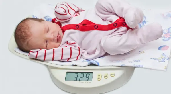 Nowe życie waży 3,29 kg. Dziecko po urodzeniu leży na wadze, ubrane w różowy pajacyk w paski.