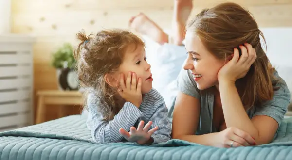 Mutter und Kind liegen auf dem Bett und sprechen. Das Kind übt emotionsregulation kinder, während die Mutter liebevoll zuhört.