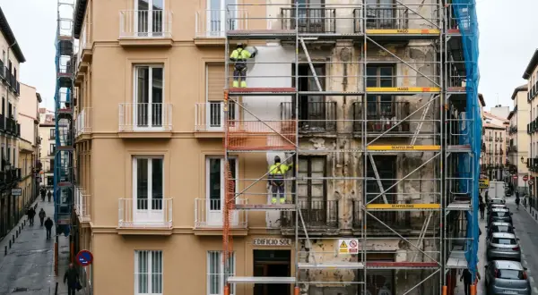 Trabajadores en andamios rehabilitan fachadas de edificios en una calle urbana.