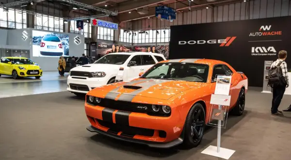 Pomarańczowy Dodge Challenger SRT Hellcat z czarnymi pasami na masce, obok białego Durango i żółtego Suzuki.