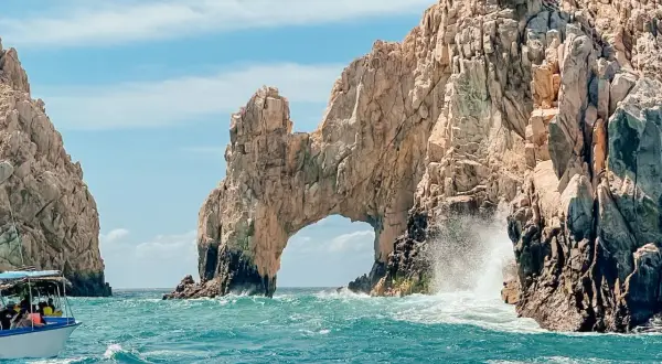 Un paseo en barco revela el Arco de Cabo San Lucas, una maravilla natural que ver en Baja California. Las olas rompen contra las rocas doradas bajo un cielo azul.