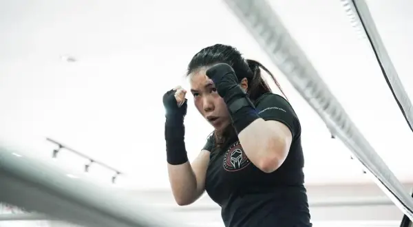 Focused woman in boxing stance, practicing her boxing workout split in a ring.