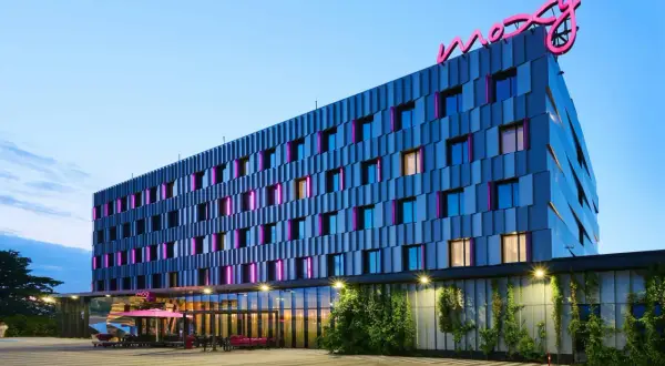 Nowoczesny hotel Moxy Hotels Pyrzowice z neonowym logo na dachu i kolorowymi podświetleniami okien.