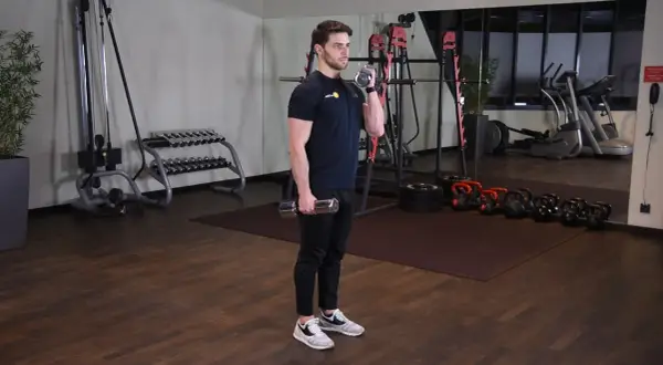 Mężczyzna wykonuje zottman curl z hantlem, ćwicząc biceps i przedramię. W tle siłownia z maszynami i ciężarami.