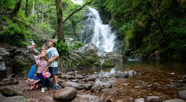 Familia toma selfie frente a la imponente cascada Xorroxin, rodeada de exuberante vegetación y rocas.