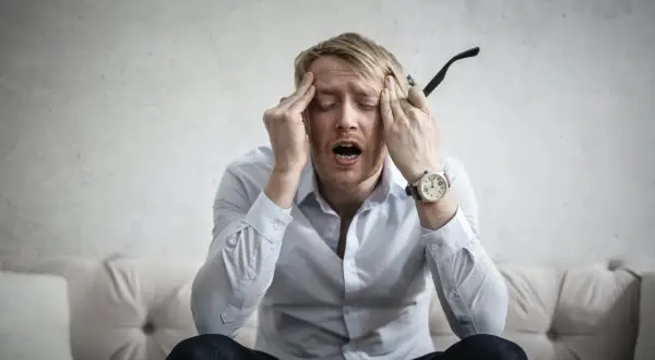 Man med händerna mot tinningarna, öppen mun, uttrycker ångest. Kanske dags för behandling av ångest.