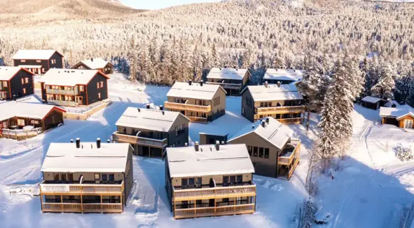 Vinterlandskap med snötäckta hus i Funäsdalens stugby. Solen lyser på de moderna stugorna och den snöklädda skogen.