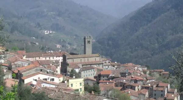 Panoramica di una villa con una basilica imponente, incastonata tra dolci colline boscose.
