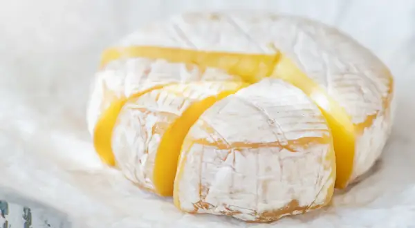 Ser camembert w ciąży, z widocznymi kawałkami, prezentuje swoje kremowe wnętrze.