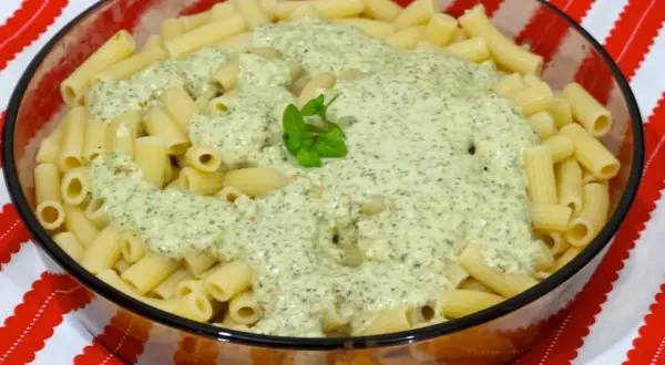 Macarrones al pesto servidos en un bol de cristal, con una hoja de albahaca fresca decorando la cremosa salsa verde.