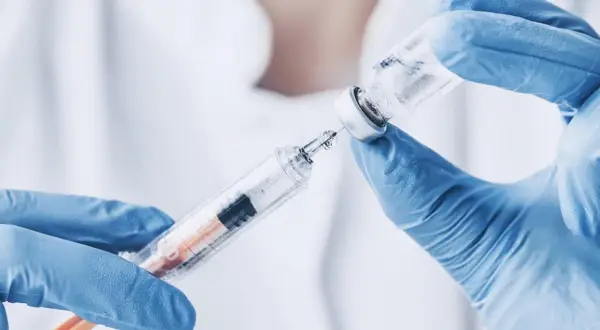 Ręce w niebieskich rękawiczkach pobierają płyn z fiolki do strzykawki. To może być propofol, środek znieczulający.