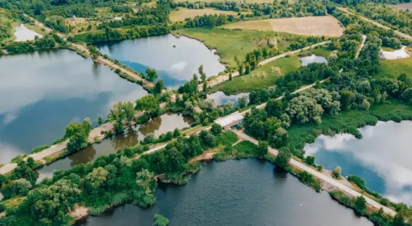 Malowniczy krajobraz z licznymi stawami i dołami, otoczony zielenią. W oddali widać pola i lasy.